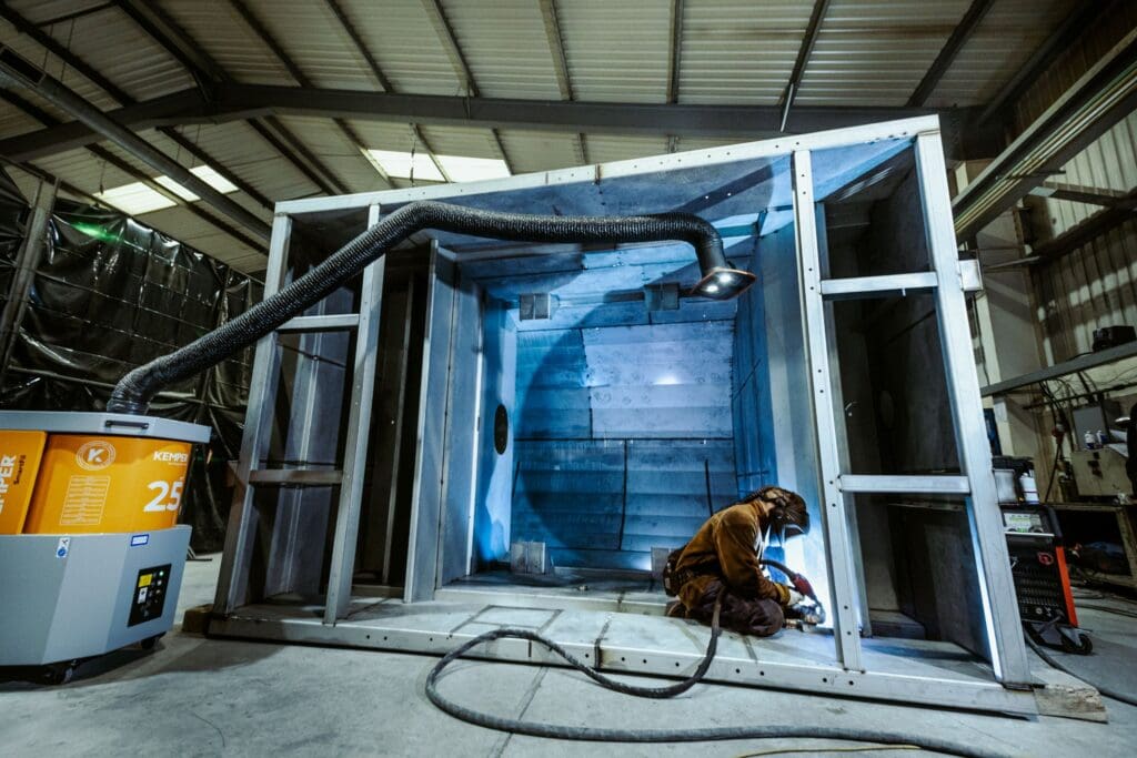 Welder working on a large steel fabrication inside an industrial workshop.